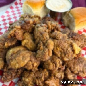 Crispy Fried Chicken Livers 12 A generous serving of crispy fried chicken livers piled high on a tray lined with checkered paper, with rolls and sauce on the side.