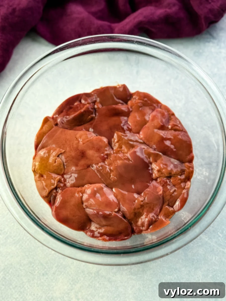 Crispy Fried Chicken Livers 4 A clear bowl filled with raw chicken livers, set on a light surface with a deep purple cloth in the background.