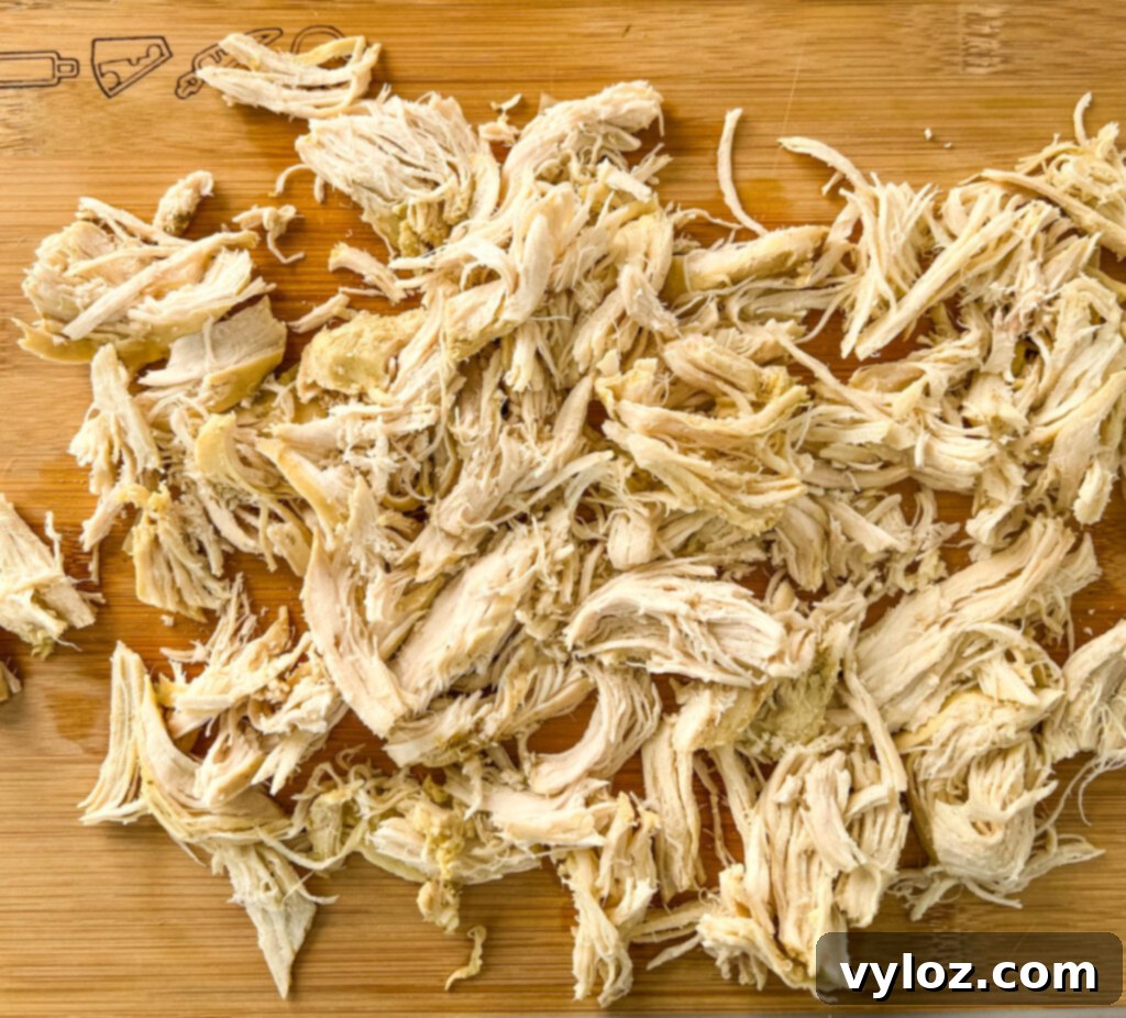 Heartwarming Chicken Noodle Soup 8 Tender shredded chicken breasts, a key component of a hearty chicken noodle soup, displayed on a rustic wooden cutting board.