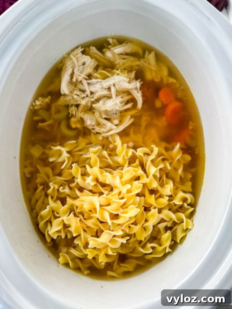 Heartwarming Chicken Noodle Soup 9 A pot of delicious chicken noodle soup, with shredded chicken and noodles simmering in a rich broth, nearly ready to serve.