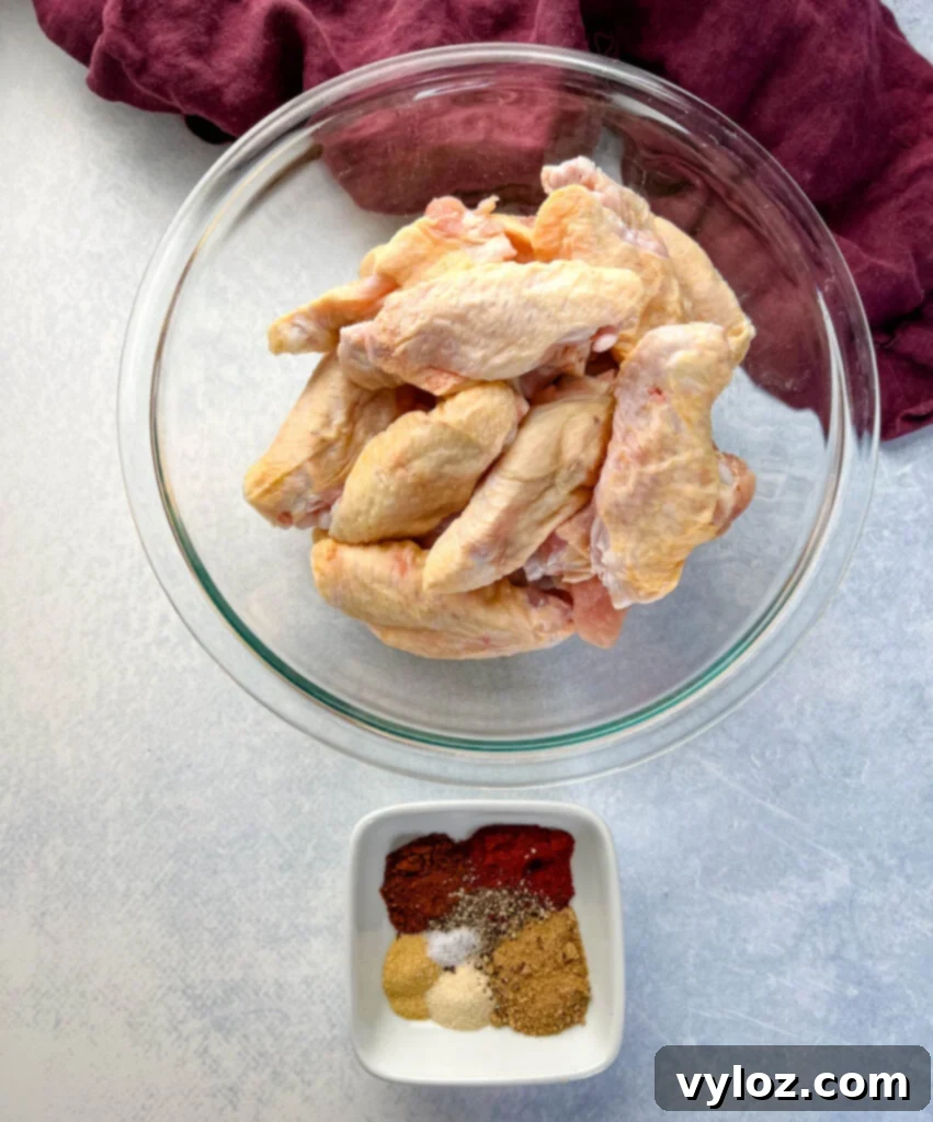 raw chicken wings in a glass bowl and a bowl with dry rub spices