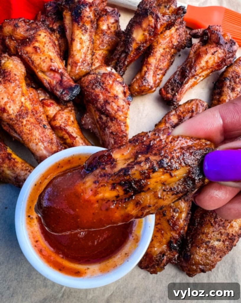 person holding Traeger smoked chicken wings dipped in BBQ sauce