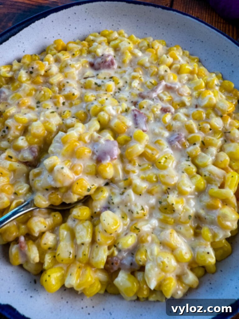 A bowl of hot Southern Soul Food Creamed Corn, garnished with fresh herbs and a spoon.