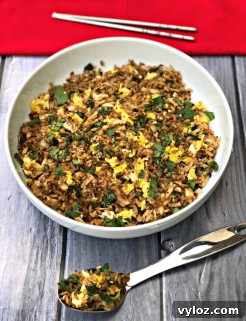 Air Fryer Crab Fried Rice neatly arranged in a white bowl, with a large spoon, a red napkin, and chopsticks on a dark wooden surface.
