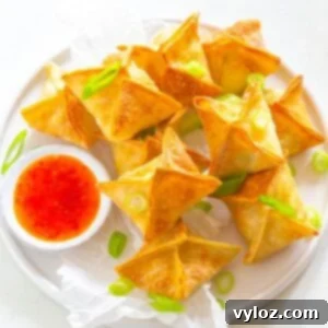 Crispy Air Fryer Crab Rangoon Delights 2 Crispy golden Air Fryer Crab Rangoons on a white plate with a side of sweet chili dipping sauce