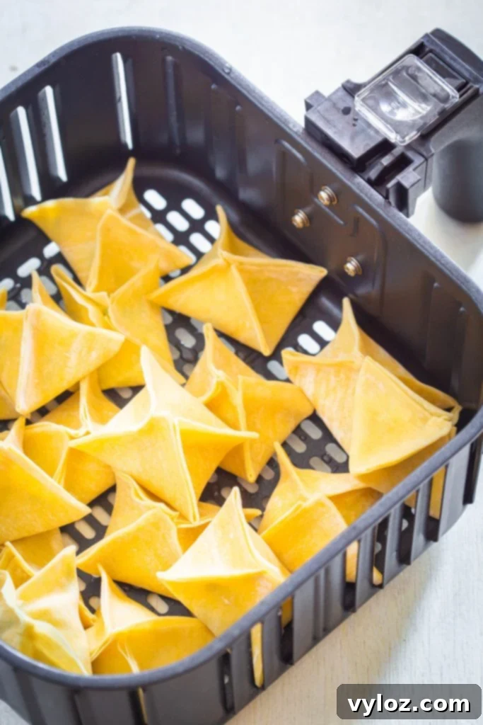 Crispy Air Fryer Crab Rangoon Delights 9 Several air fryer crab rangoons arranged in an air fryer basket, cooking to a golden crisp.