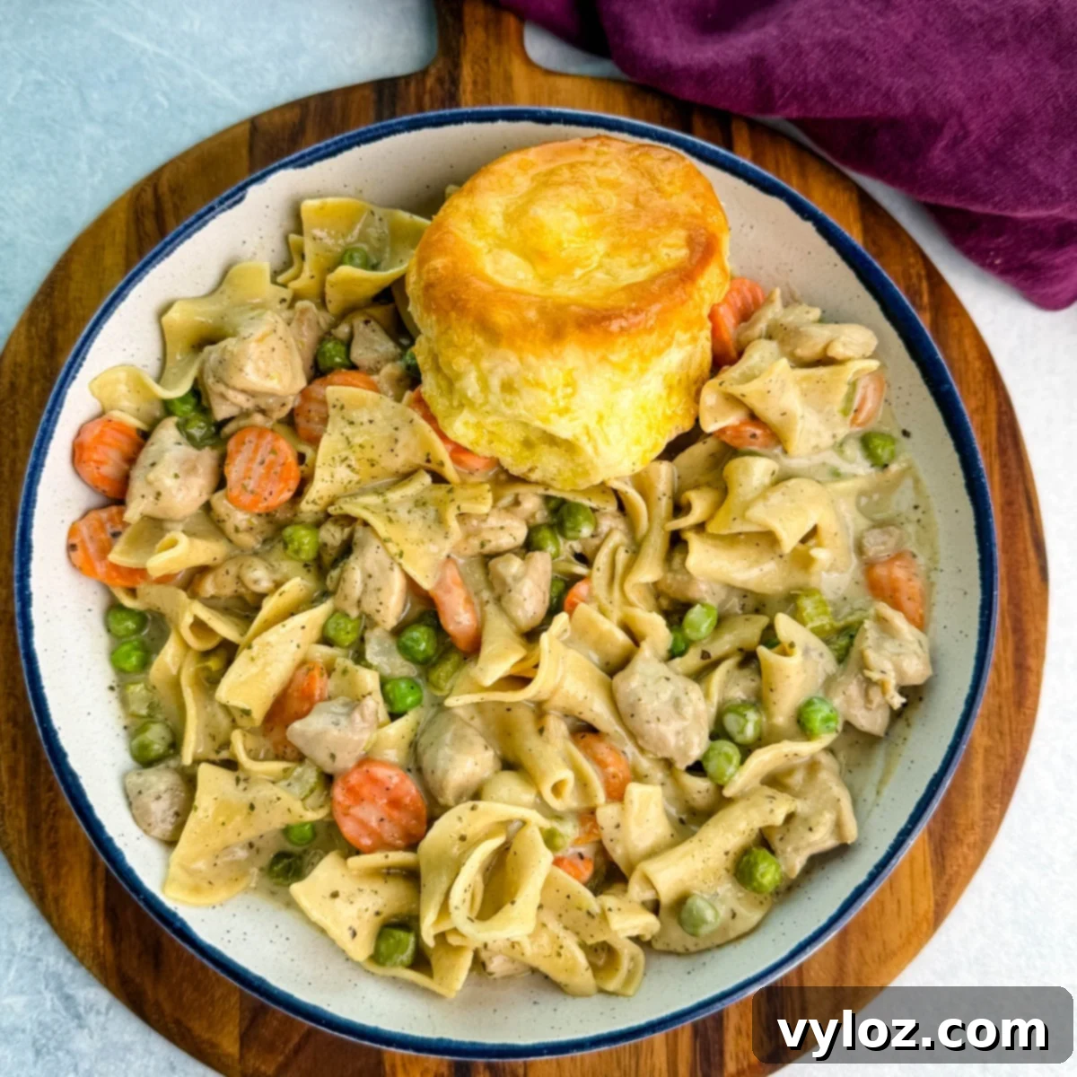 Close-up of a creamy one-pot chicken pot pie casserole with egg noodles, peas, and carrots served in a cast-iron skillet topped with golden biscuits.