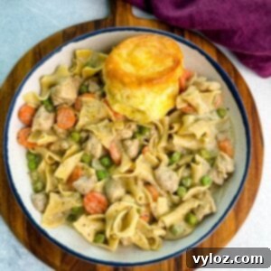 Close-up of a creamy one-pot chicken pot pie casserole with egg noodles, peas, and carrots served in a cast-iron skillet topped with golden biscuits.