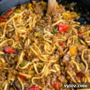 Close-up shot showing saucy Mongolian ground beef noodles with red peppers, mushrooms, and bits of green vegetables, highlighting the glossy, caramelized texture of the sauce.