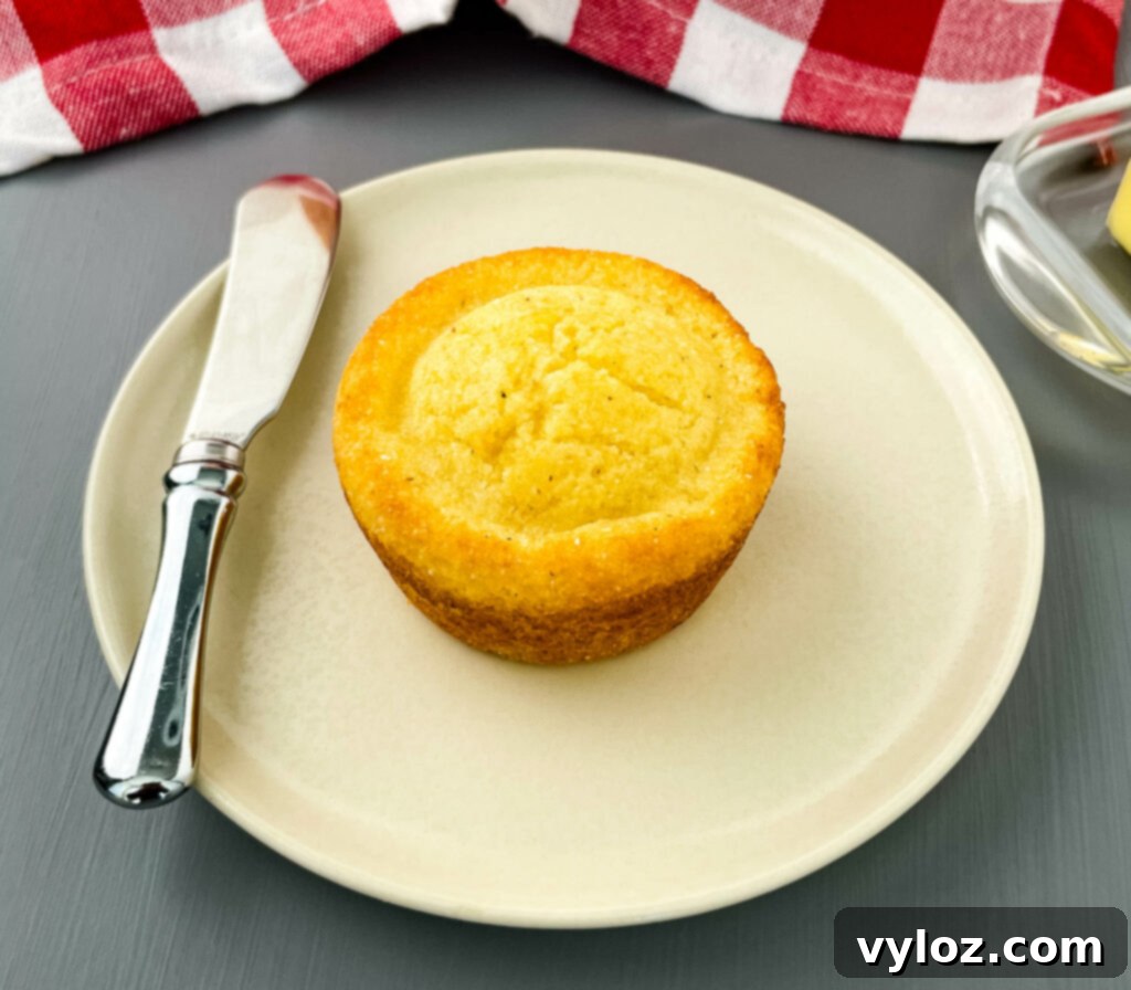 A single warm cornbread muffin presented elegantly on a white plate, showcasing its golden color and inviting texture.