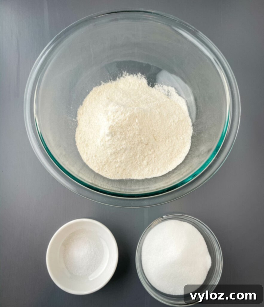 Three glass bowls displaying dry ingredients: fine self-rising cornmeal, a pinch of salt, and a scoop of sweetener, ready for baking.
