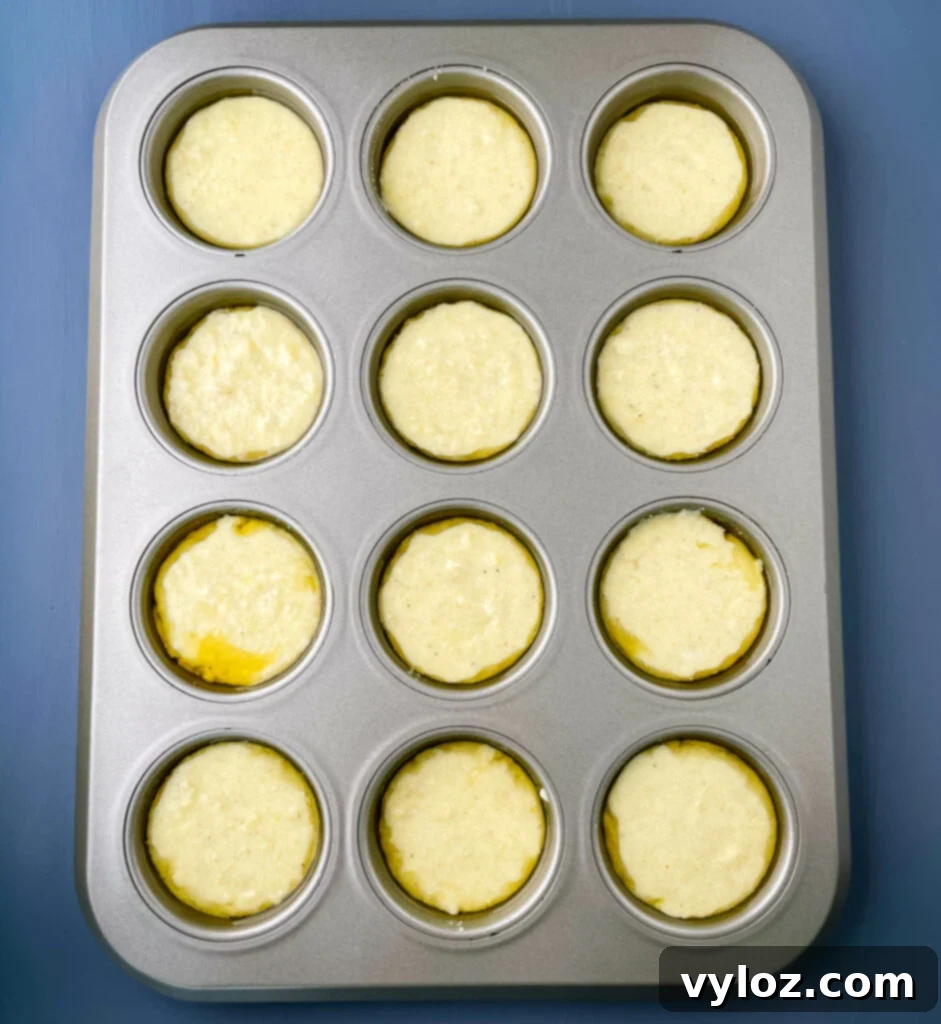 Close-up shot of golden cornbread batter filling a muffin tin, ready for baking in the oven.