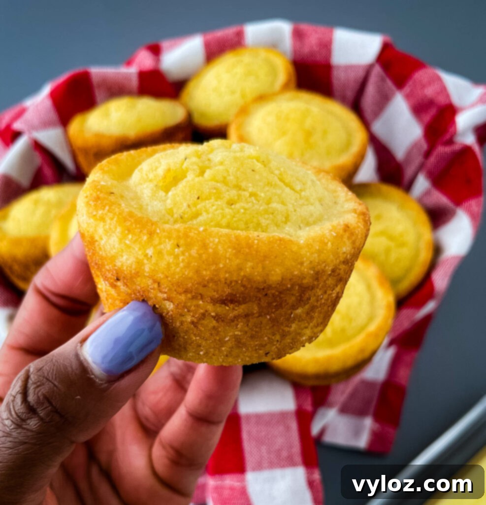 A hand holding a warm, golden cornbread muffin, showing its fluffy texture and inviting aroma.