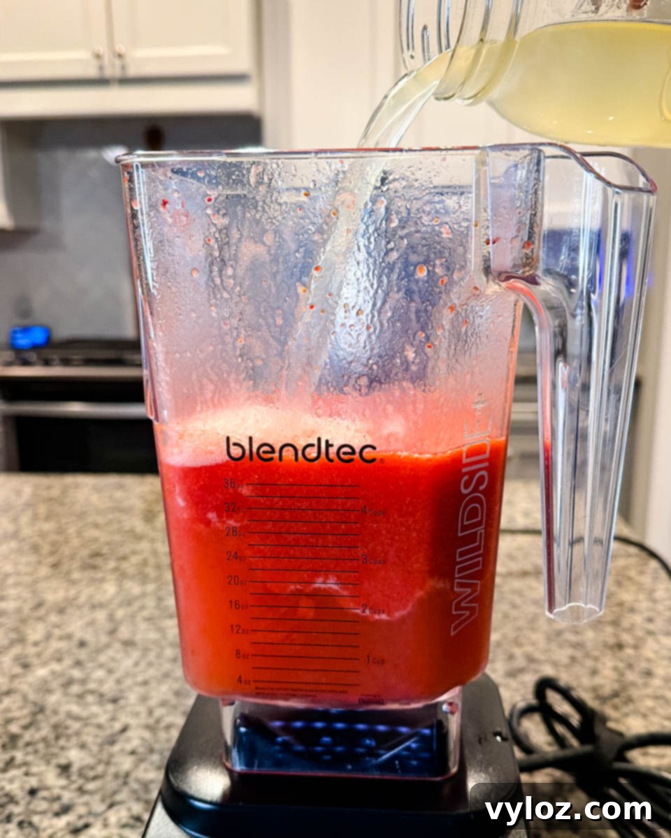 Hennessy Midnight Slush 5 Pineapple juice being poured into a Blendtec blender containing frozen strawberry mixture, preparing for the Hennessy slushie.