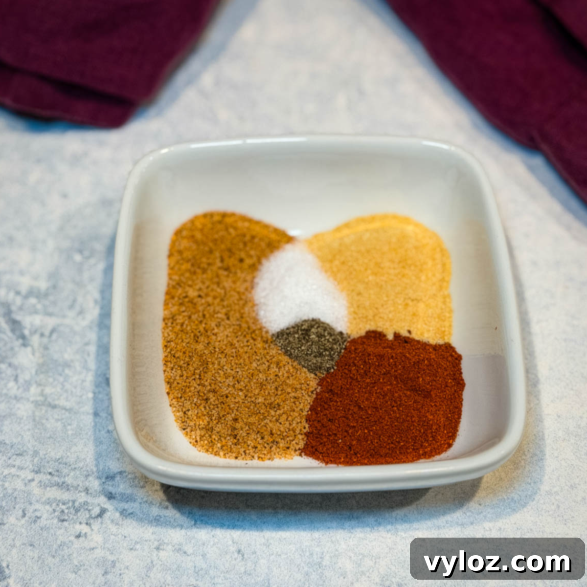 A small white bowl filled with a rich, reddish-brown fried chicken seasoning mix, showcasing the blend of spices. The texture suggests a fine grind, ready to infuse flavor.