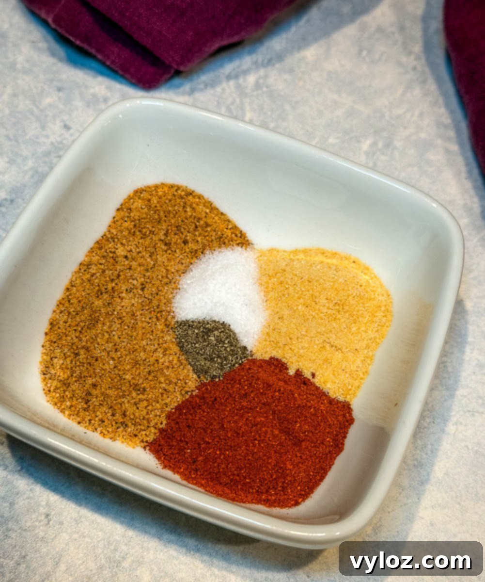 A small white bowl filled with a rich, reddish-brown fried chicken seasoning mix, showcasing the blend of spices. The texture suggests a fine grind, ready to infuse flavor.