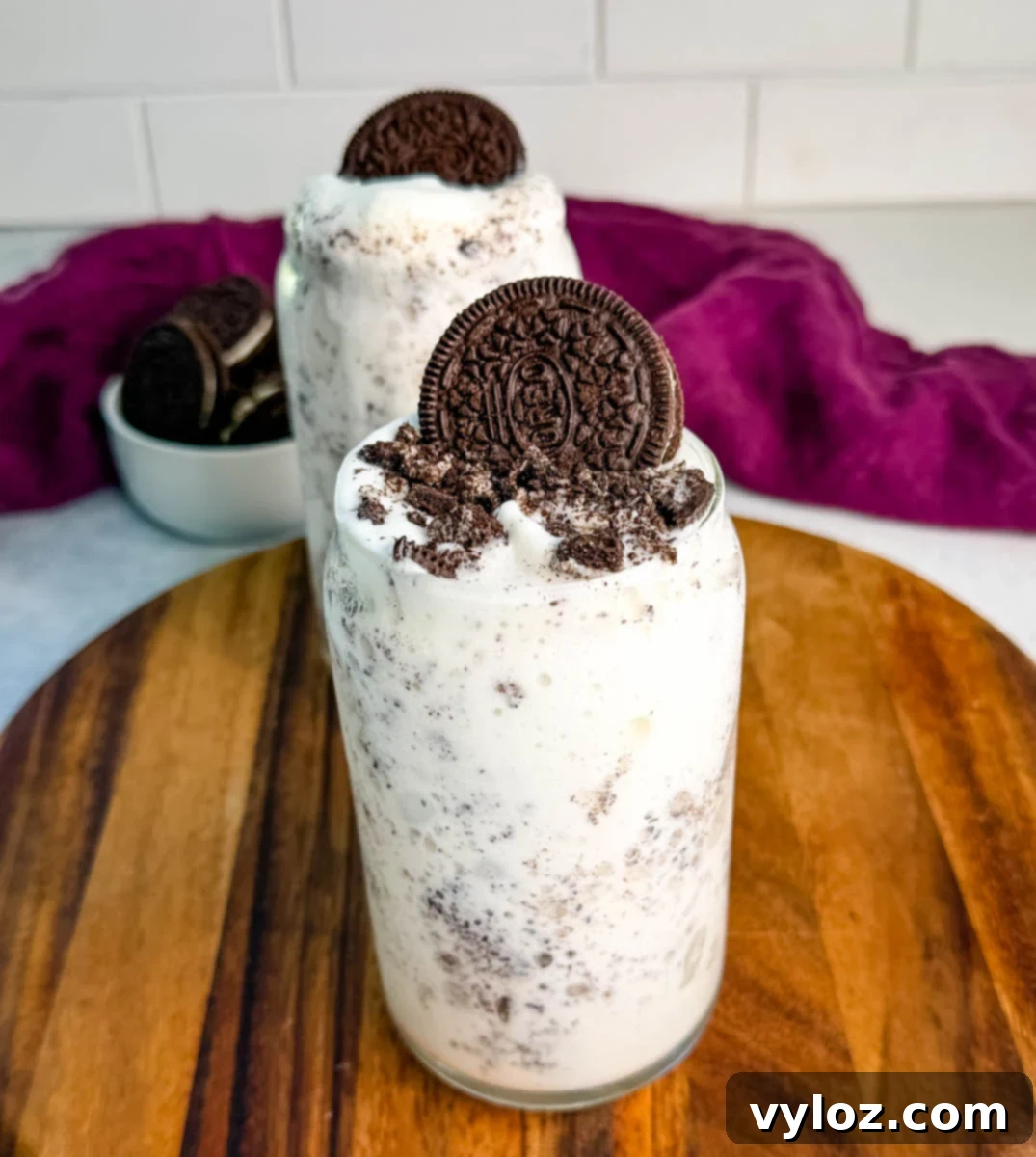Stealthy Slushy Delight 2 A tall glass of Oreo McFlurry-style Ninja Slushi topped with crushed cookies and a whole Oreo on top, sitting on a wooden board with a purple cloth in the background.