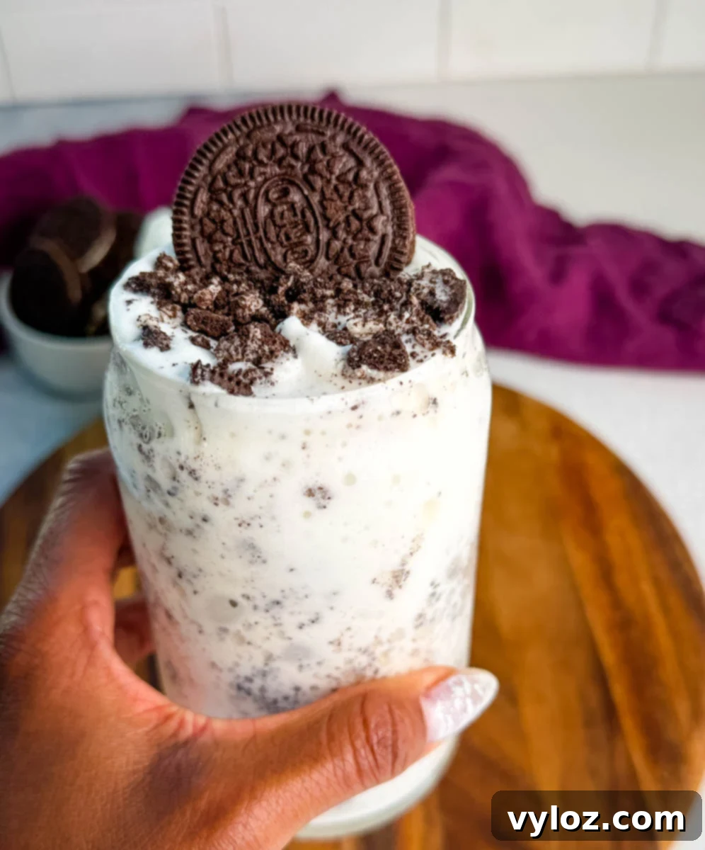 Stealthy Slushy Delight 11 A hand holding a glass filled with a creamy Oreo Ninja Slushi McFlurry topped with crushed cookies and a whole Oreo cookie.