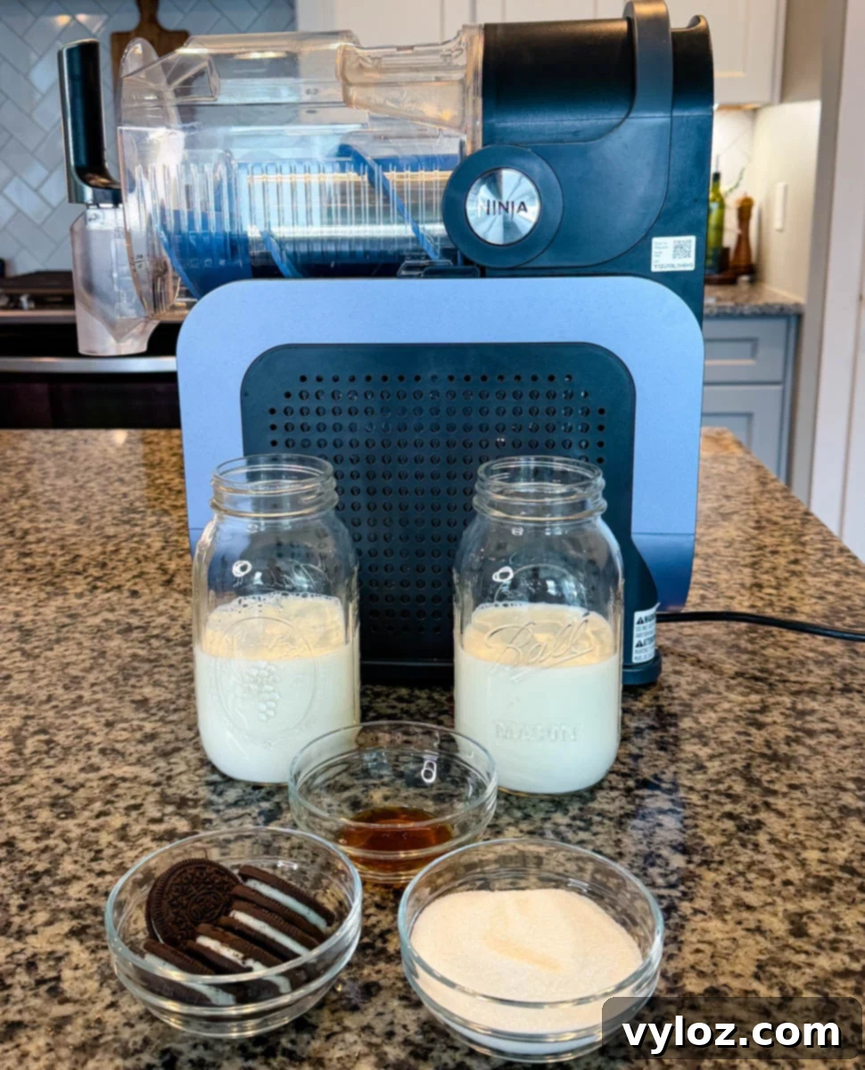 Stealthy Slushy Delight 3 Ninja Slushi machine on a kitchen counter with ingredients for a McFlurry, including two jars of milk, vanilla extract, sugar, and Oreo cookies in small glass bowls.