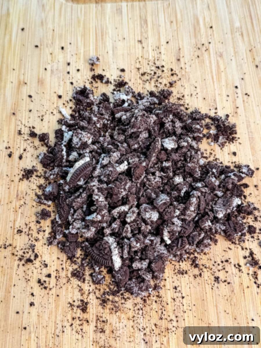 Stealthy Slushy Delight 7 Crushed Oreo cookies on a wooden cutting board, showing cookie crumbs and cream filling pieces.