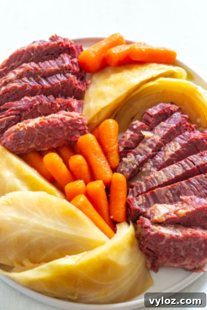 Instant Pot Corned Beef and Cabbage 2 Generous serving of tender corned beef, bright carrots, and crisp cabbage on a white plate, ready to be enjoyed.