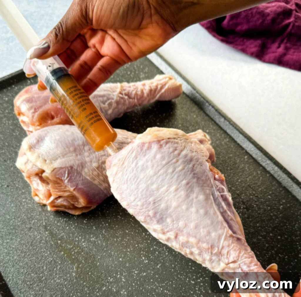 Person injecting raw turkey leg with butter using a meat injector