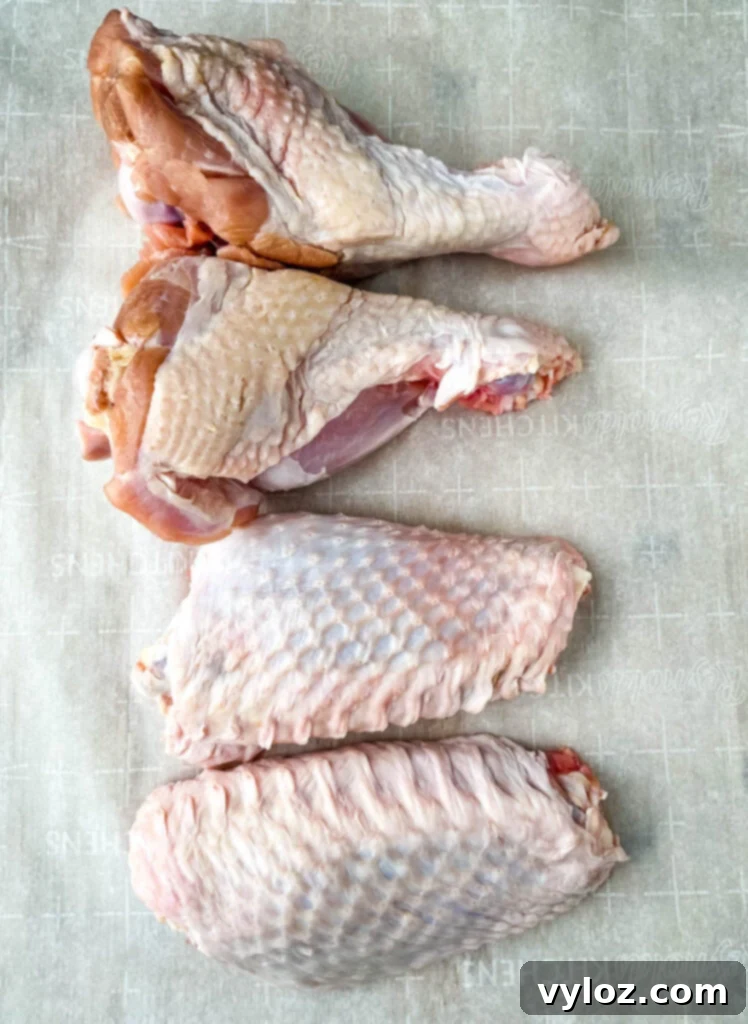 Raw turkey wings arranged neatly on parchment paper, awaiting seasoning.