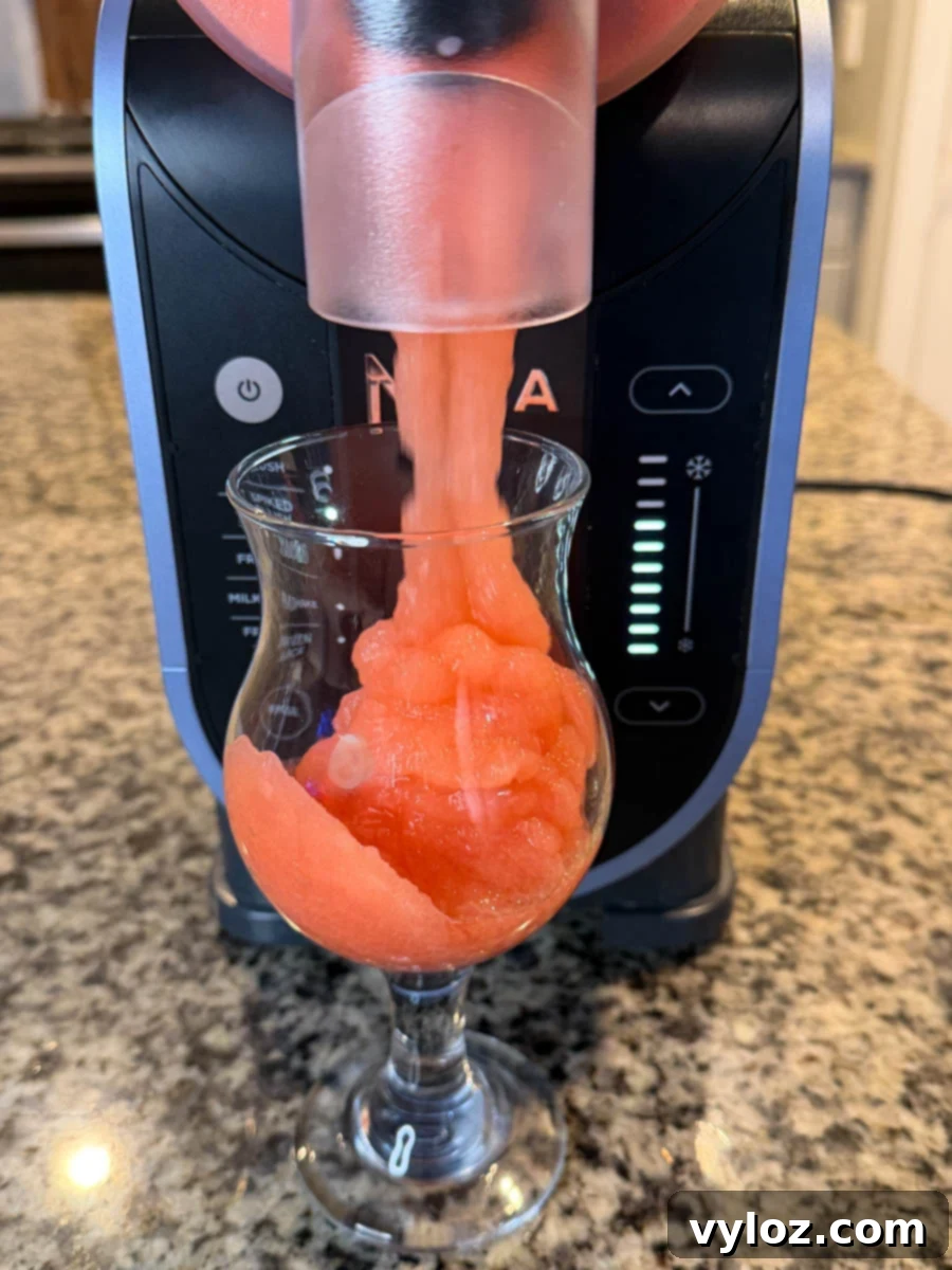 Dispensing the finished frozen rum punch from the Ninja Slushi machine into a glass.