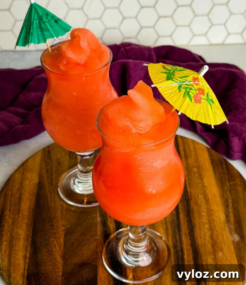 Two glasses of frozen Ninja Slushi Rum Punch topped with mini paper umbrellas on a wooden board.