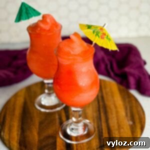 Two glasses of frozen Ninja Slushi Rum Punch topped with mini paper umbrellas on a wooden board.