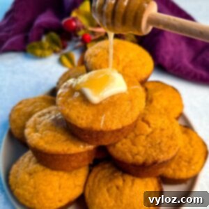 A stack of golden-brown Jiffy sweet potato cornbread muffins on a plate, topped with melting butter and drizzled with honey for a glossy, irresistible finish.