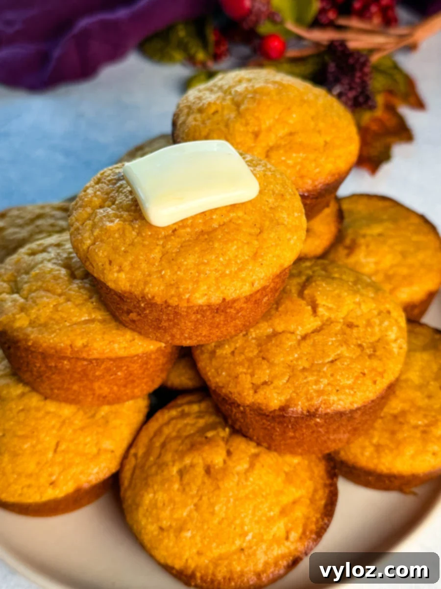 A close-up of warm sweet potato cornbread muffins stacked on a plate, with a melting square of butter on top.