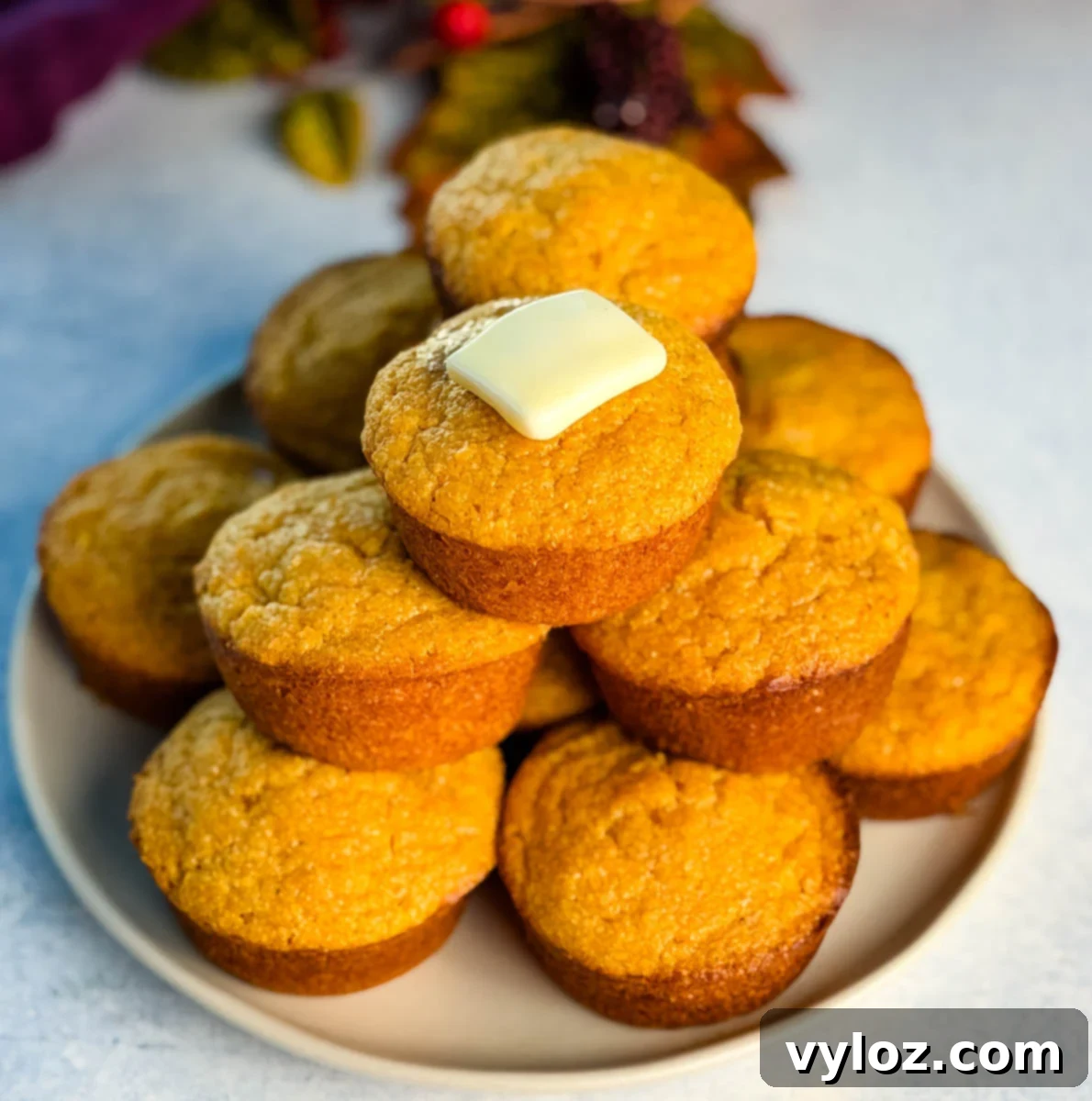 A full plate stacked with golden Jiffy sweet potato cornbread muffins, featuring a pat of butter melting on the top muffin.