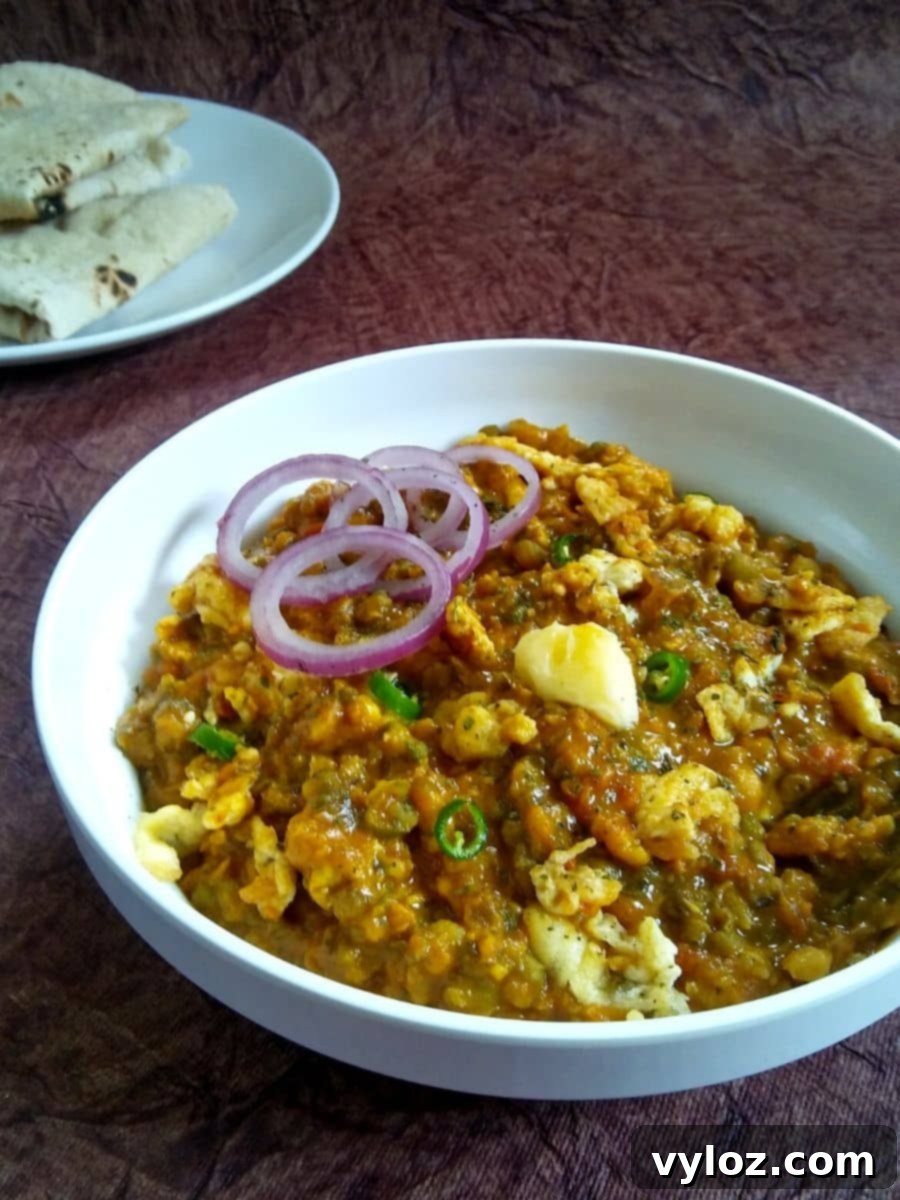 Effortless Bengali Egg Tadka 2 Egg Tadka served in a bowl topped with onion rings.