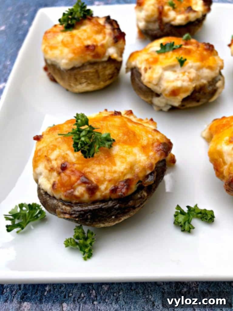 Golden Cheesy Air Fryer Mushrooms 2 Cooked air fryer cheese stuffed mushrooms on a white plate, garnished with fresh herbs
