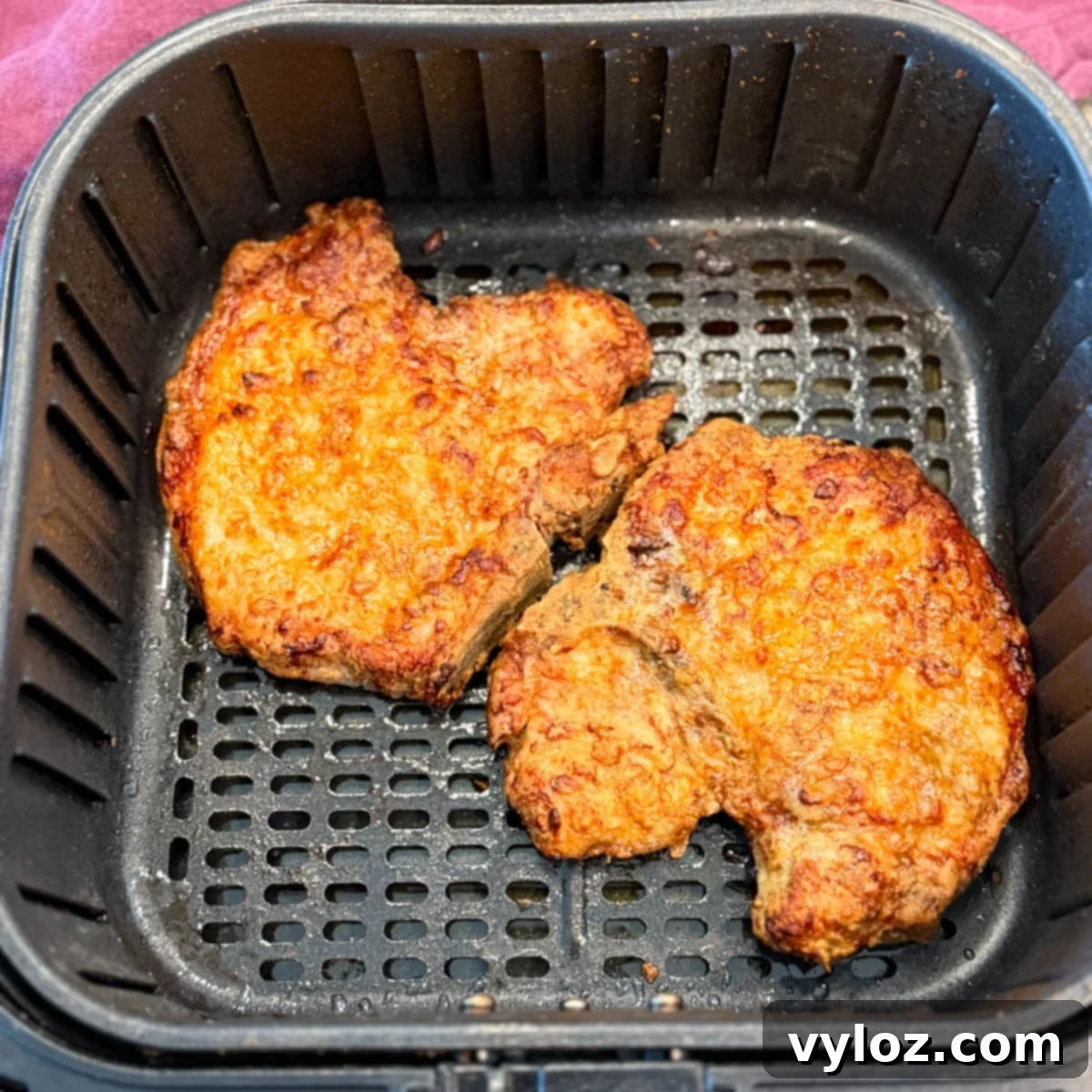 Two golden, crispy breaded pork chops sitting in an air fryer basket after cooking.