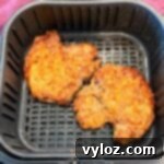 Two golden, crispy breaded pork chops sitting in an air fryer basket after cooking.