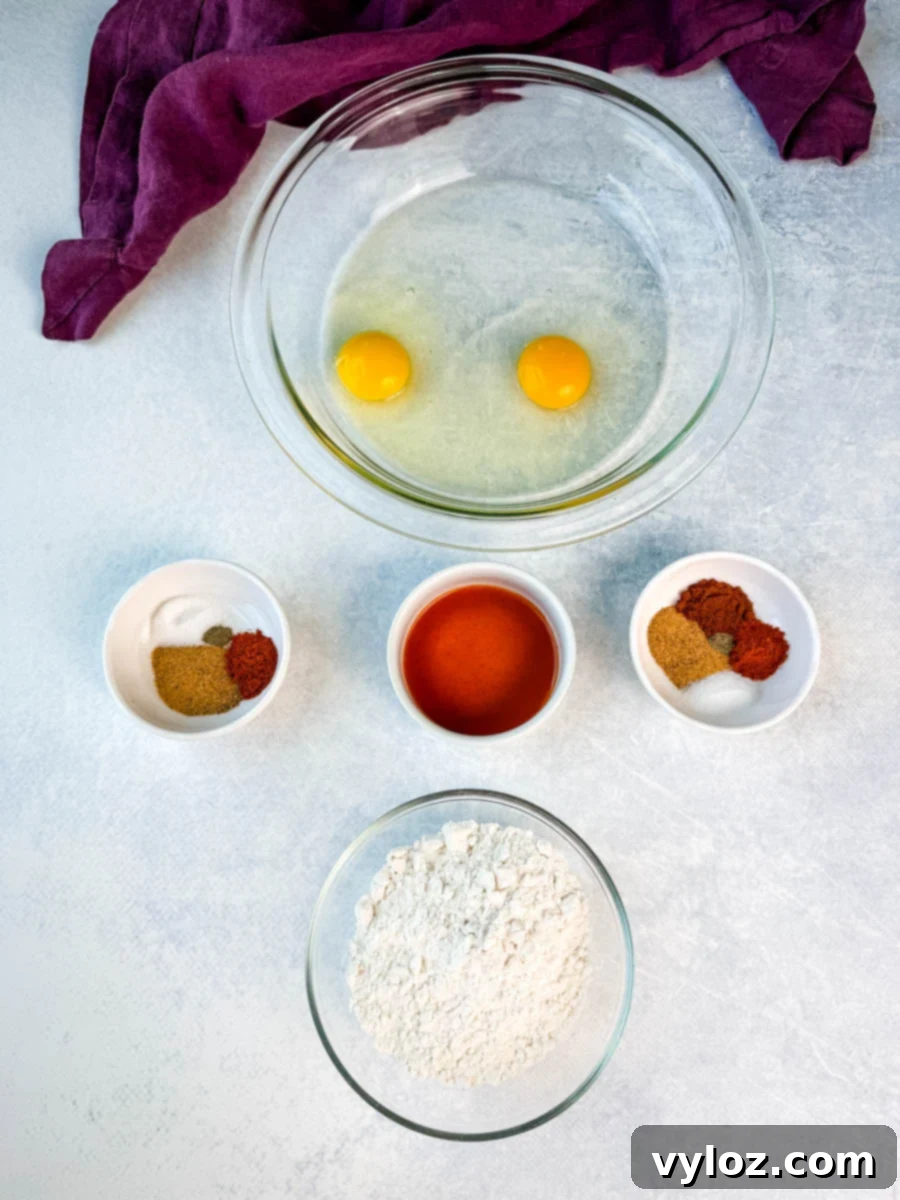 Overhead shot of ingredients for fried pork chops, including two eggs in a bowl, flour, hot sauce, and various spices in small bowls.