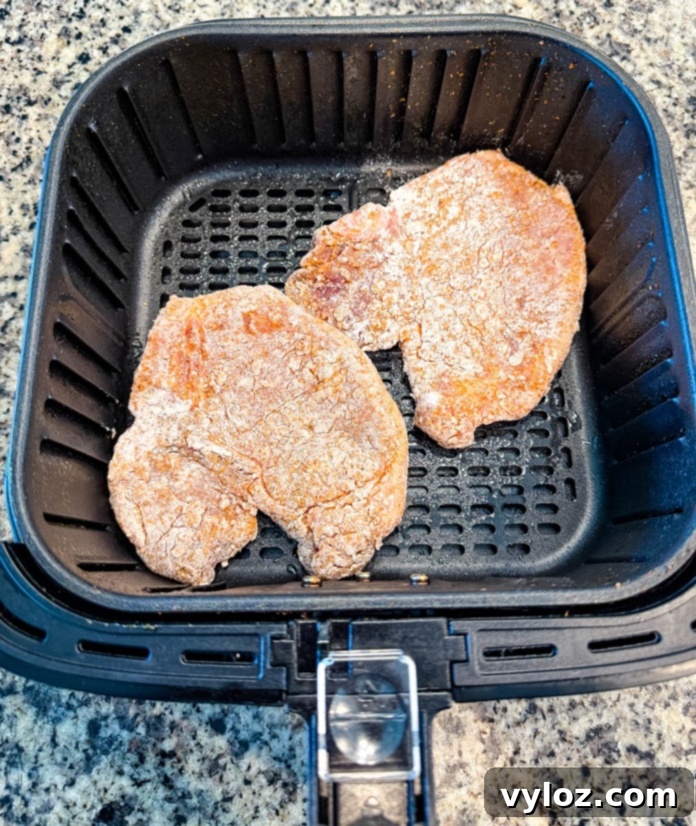 Two raw, breaded pork chops placed in the air fryer basket before cooking.