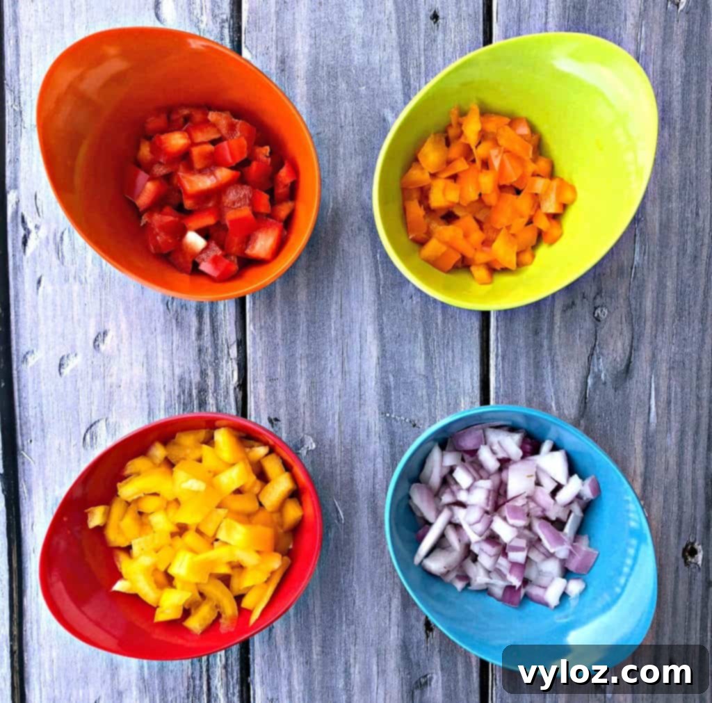 Diced red, orange, and yellow bell peppers along with red onions in multi-colored bowls, ready for the egg roll filling.
