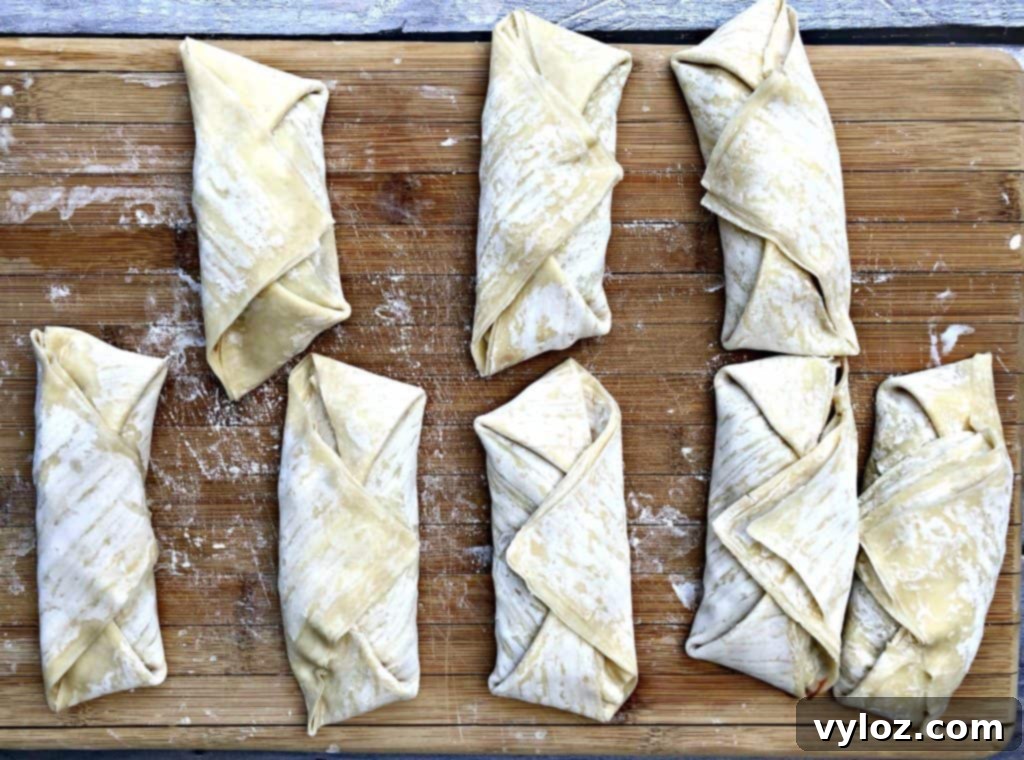 Eight uncooked egg rolls neatly arranged in their wrappers, prepared for air frying.