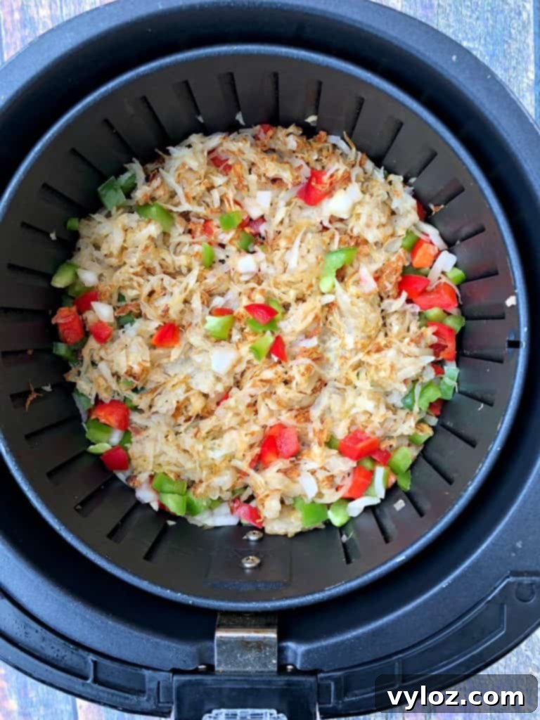 Perfectly Crispy Air Fryer Hash Browns 5 hashbrowns cooking in an air fryer with chopped vegetables scattered on top