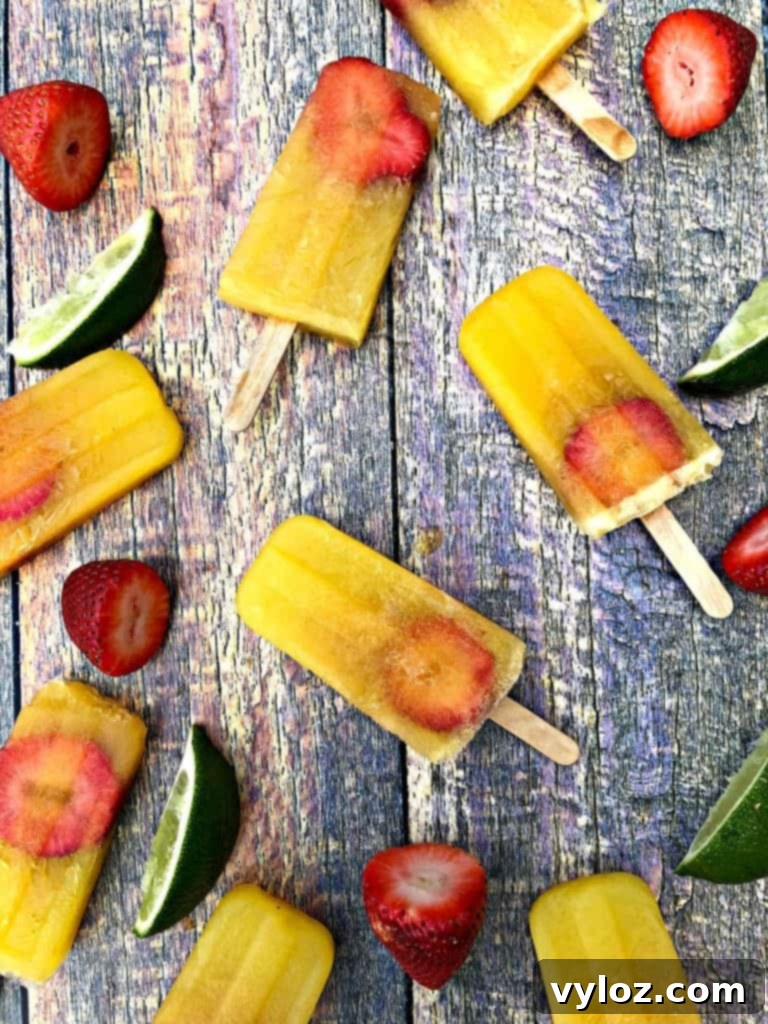 Adult Margarita Pops 2 Freshly made strawberry margarita popsicles on a wooden surface with sliced limes and whole strawberries scattered around