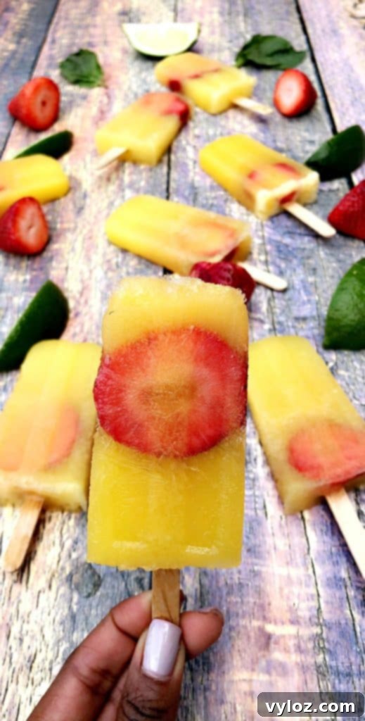 Adult Margarita Pops 11 A close-up of a margarita popsicle being held, with a blurred background of limes and strawberries