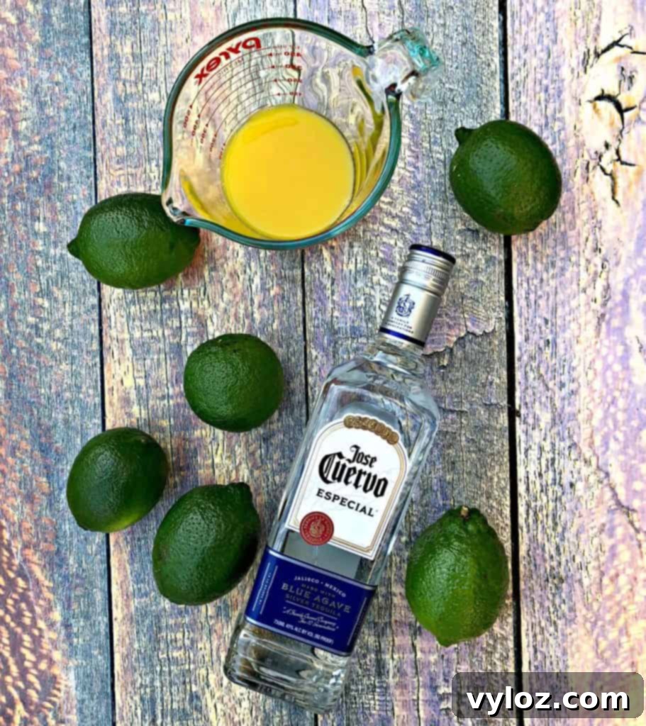 Adult Margarita Pops 3 Ingredients for margarita popsicles: limes, tequila bottle, and orange juice in glasses on a flat surface