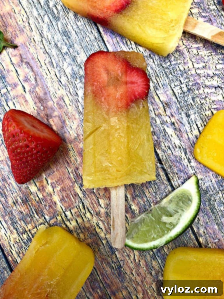 Adult Margarita Pops 9 Close-up of three margarita popsicles on a flat surface with limes and strawberries