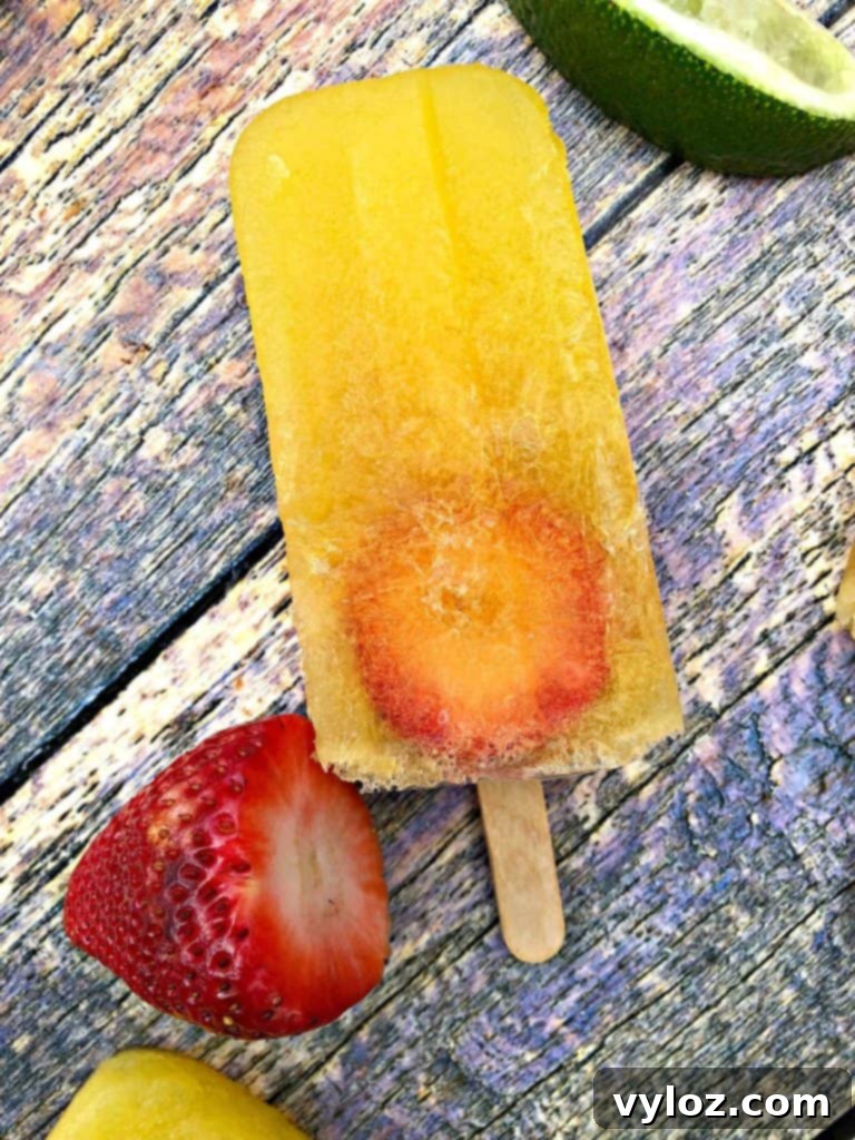 Adult Margarita Pops 10 A single margarita popsicle on a flat surface with blurred strawberries and limes