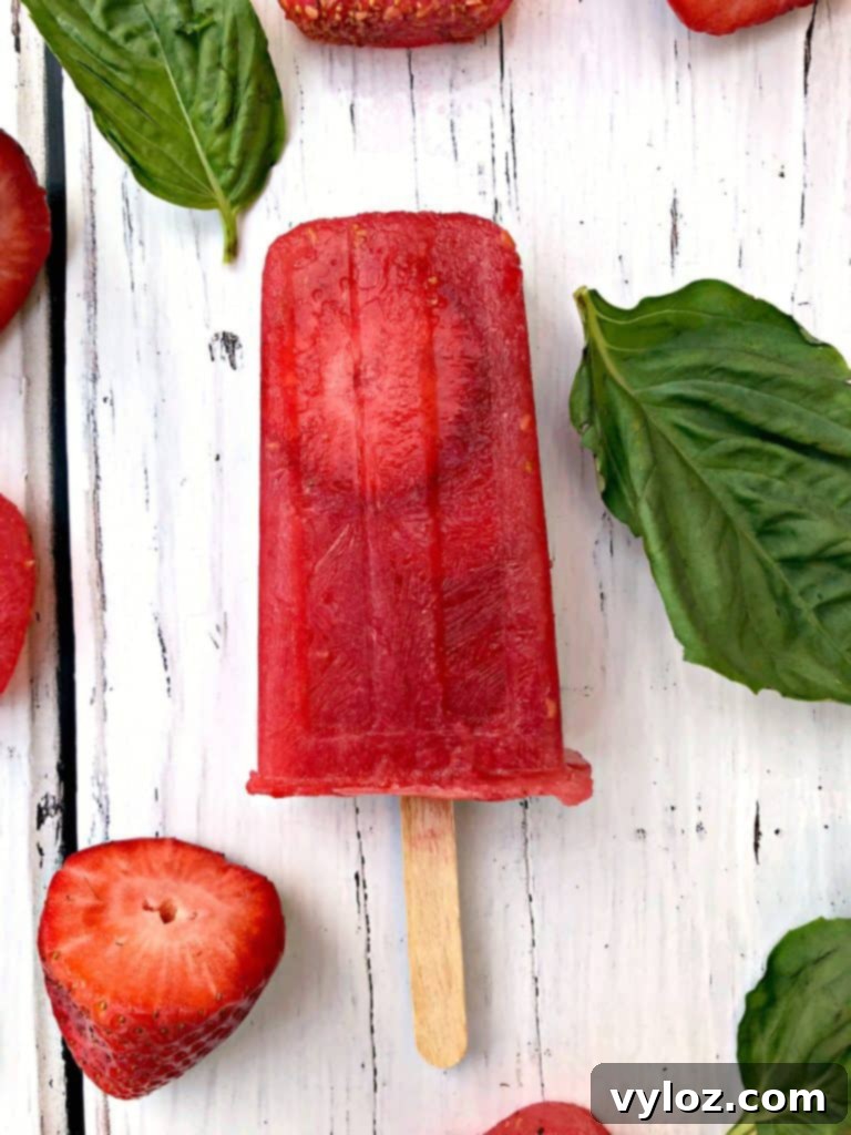 Vibrant Rosé wine popsicles garnished with fresh basil and strawberries, ready to be enjoyed as a refreshing boozy treat.