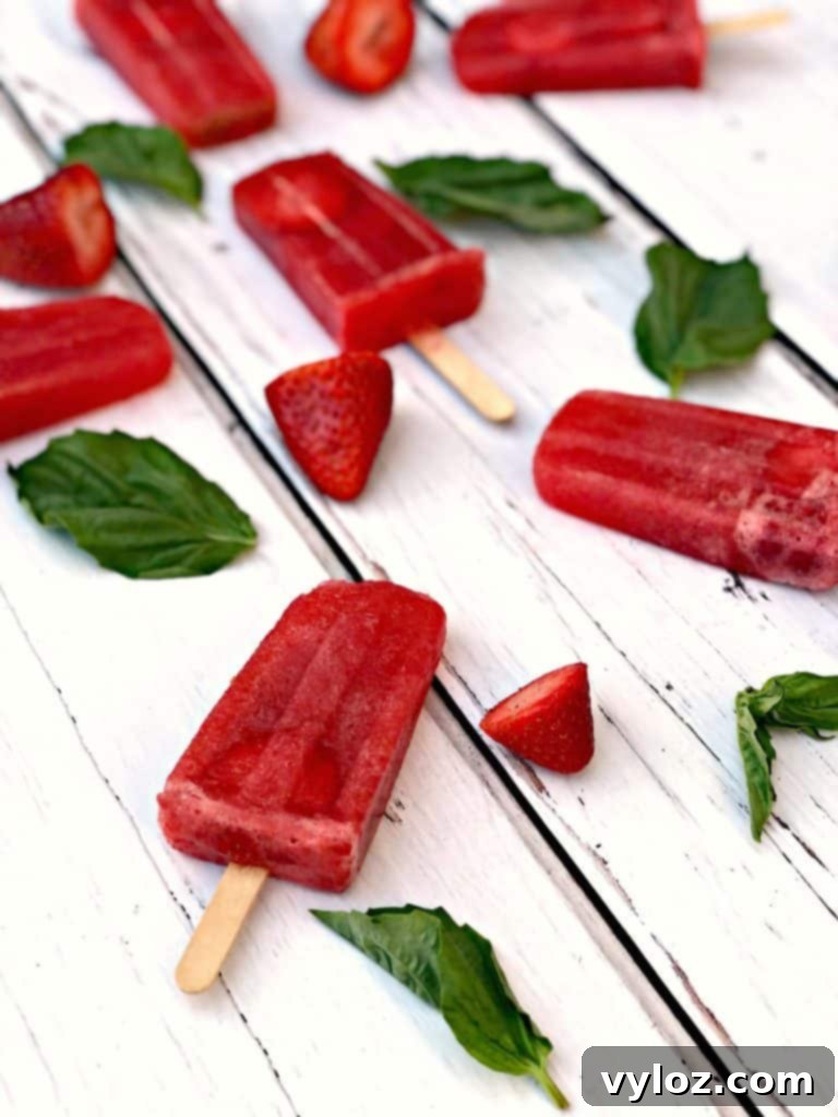 Three Rosé wine popsicles, garnished with fresh strawberries and basil, arranged on a dark background.