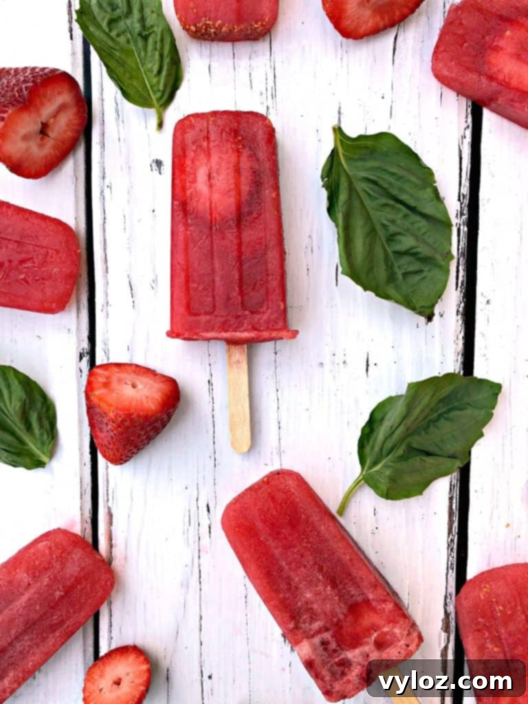 Two Rosé wine popsicles with strawberries and basil, one held in a hand, showcasing their refreshing appeal.
